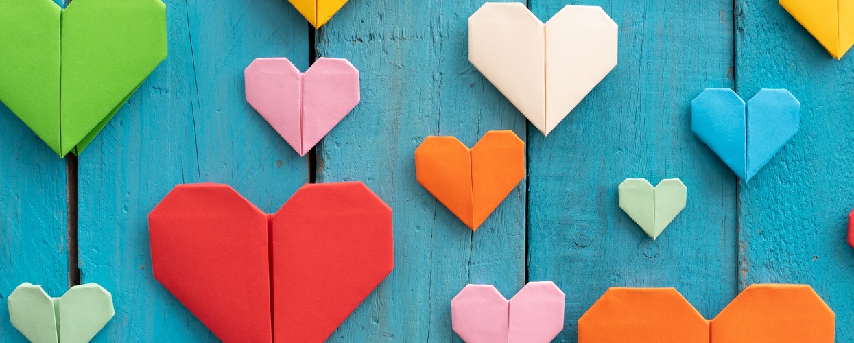 Flera färgglada origamihjärtan i olika storlekar på en blå träbakgrund.
