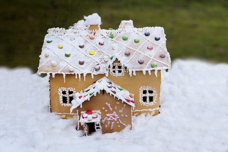 Ett dekorerat pepparkakshus med vit glasyr och färgglada godisbitar står på snö.