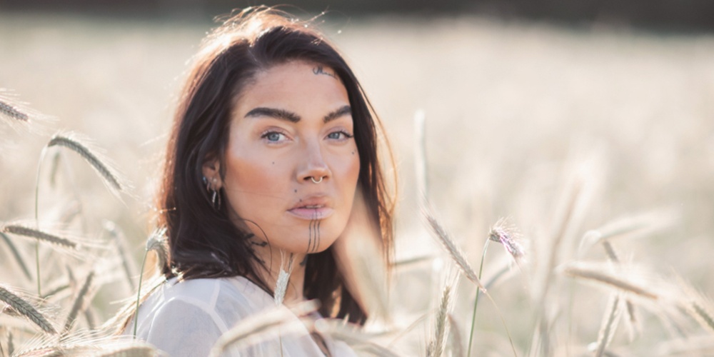 Person med långt hår står i ett fält av vete en solig dag. Ansiktet är suddat.