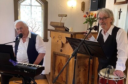Två musiker uppträder i en liten kyrka, en spelar keyboard och den andra trumma, båda vid mikrofoner.
