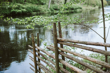 En trästaket står vid kanten av en lugn flod omgiven av grönskande natur.