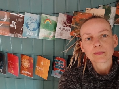 Person med blont hår i dreadlocks framför en vägg med färgglada kort upphängda på snören.