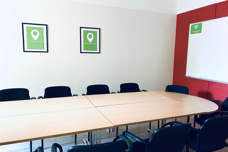 Ett tomt konferensrum med ett ovalt bord, svarta stolar och tavlor på väggen.