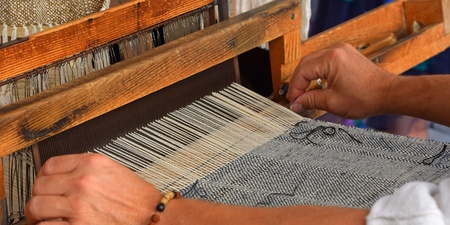 Närbild av händer som väver tyg på en traditionell vävstol.