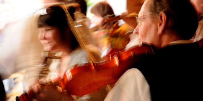 Suddig bild av personer som spelar fiol i en livlig miljö, rörelseoskärpa dominerar.