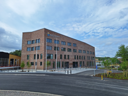 Modern tegelbyggnad med skylten Borås Tingsrätt, omgiven av nyplanterade träd och en asfalterad väg.