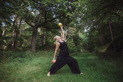 Person i svarta kläder gör yoga eller stretching med frukt i händerna i en grön skog.