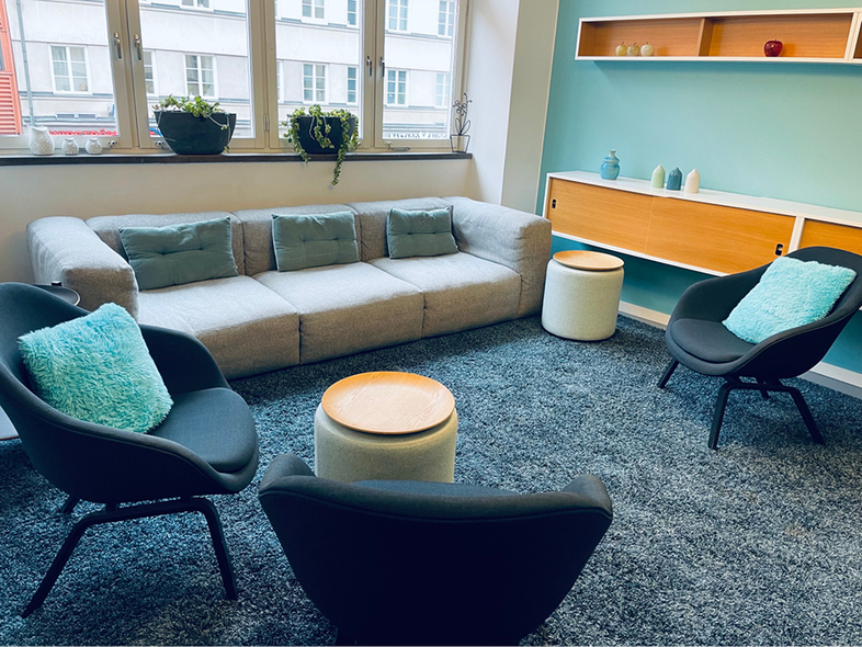 Ett modernt vardagsrum med grå soffa, två svarta fåtöljer, blå kuddar och ett blått väggskåp.