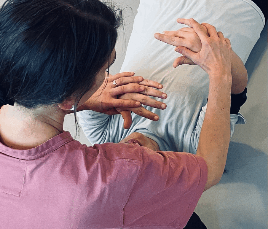 Två personer utför en handövning, en sitter och en ligger ner, händerna är i fokus.