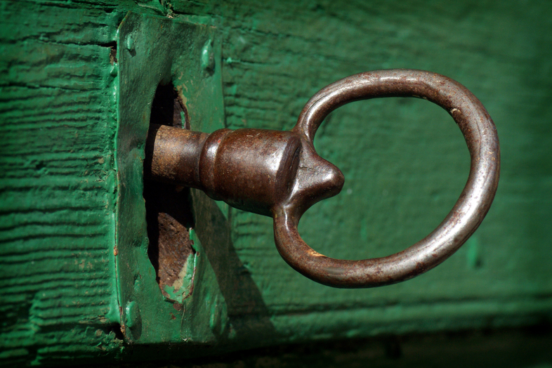 En gammal metallnyckel sitter i ett grönt, väderbitet tränyckelhål.
