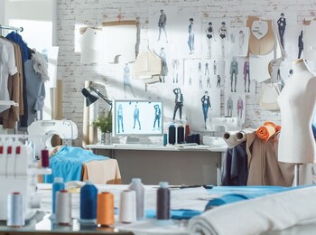 Ett kreativt modeateljé med symaskiner, tyg, provdocka och skisser på väggen.