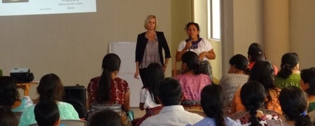 Två kvinnor står framför en grupp sittande personer under en presentation i ett ljust rum.