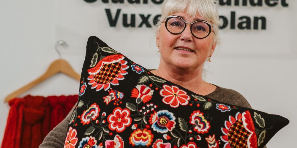 Kvinna med glasögon håller en kudde med färgglatt blommönster framför sig.
