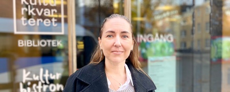 Kvinna står utanför en byggnad med skyltar för bibliotek och bistro.