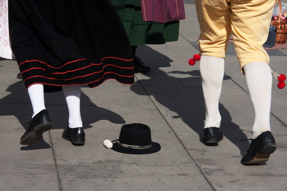 Två personer i traditionella folkdräkter dansar utomhus, en svart hatt ligger på marken mellan dem.