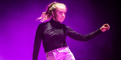 En person dansar barfota på en scen med lila ljus och rökeffekter.