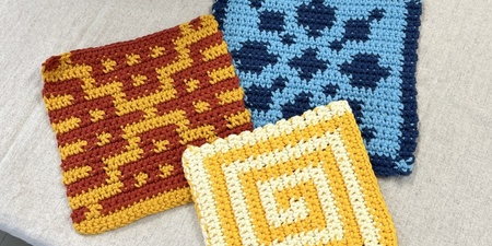 Tre virkade grytlappar med olika mönster och färger ligger på ett bord.