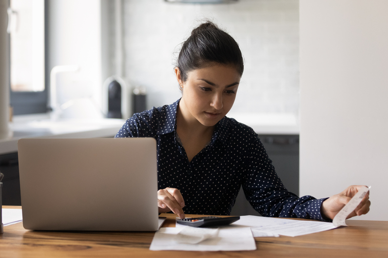 Kvinna sitter vid ett bord med laptop, papper och miniräknare, fokuserad på arbete.