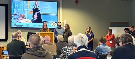 Möte eller presentation i konferensrum med flera personer, en talare vid podiet och publik som lyssnar.