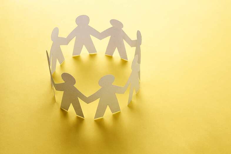 Illustration med urklippta pappersgubbar som sitter ihop i händerna och bildar en ring, gul bakgrund.