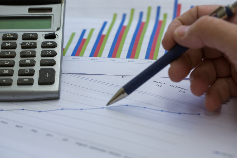 En hand håller en penna över ett papper med diagram och en miniräknare bredvid.