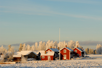 Röda trähus på snötäckt landsbygd med frostiga träd i bakgrunden under klar himmel.