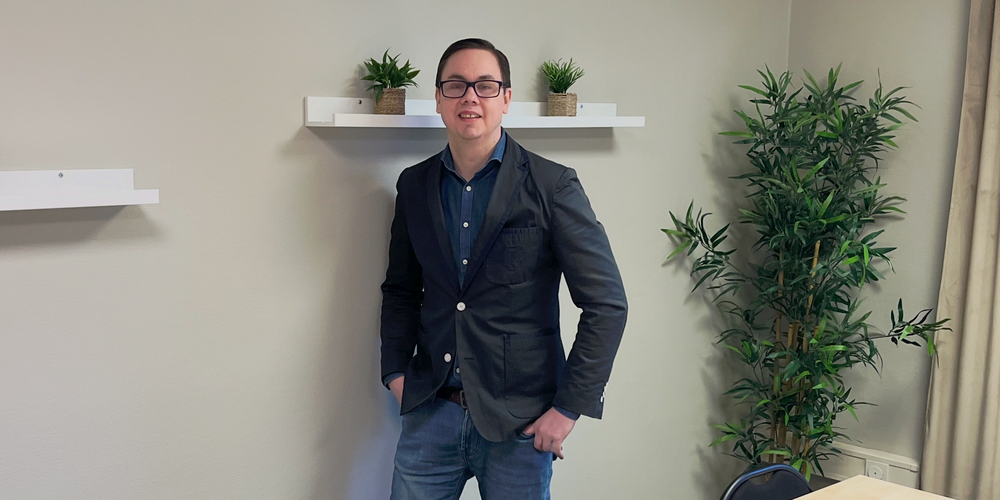 En person står vid väggen i ett mötesrum med bord, stolar, växter och hyllor med krukväxter.