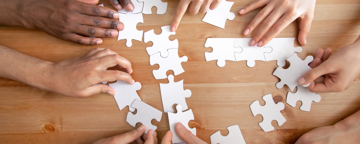 Flera händer samarbetar för att lägga ett pussel på ett trägolv.