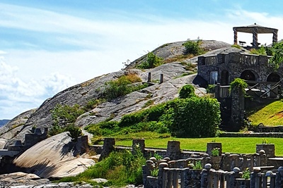 Stenbyggnader och valv på en grön kulle vid havet under en klarblå himmel.