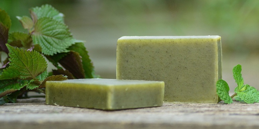 Två gröna tvålar ligger på ett träbord utomhus med gröna blad bredvid.