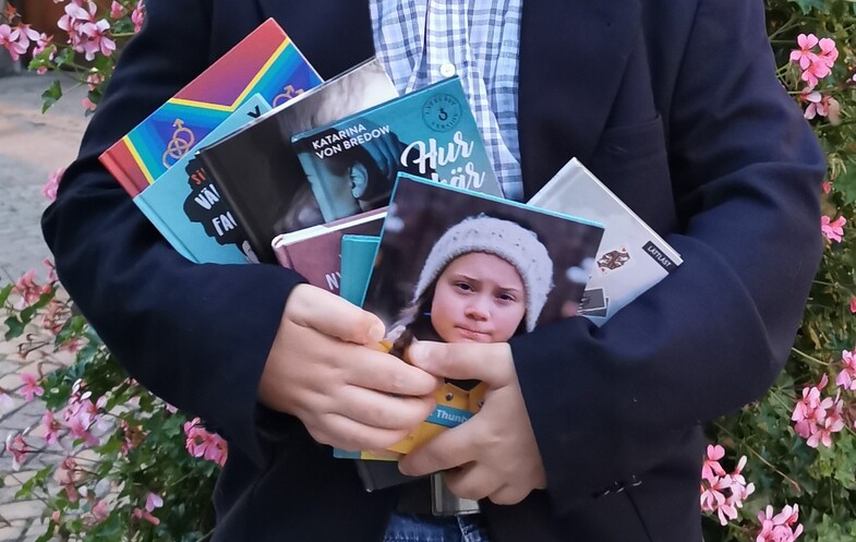 En person som håller en mängd böcker i famnen.