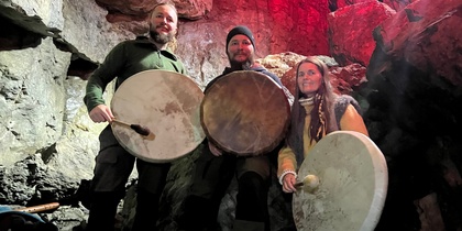 Tre personer med trummor sitter i en grotta med röd belysning på klipporna.