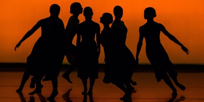 Sex dansare i silhuett poserar mot en orange bakgrund på en scen.