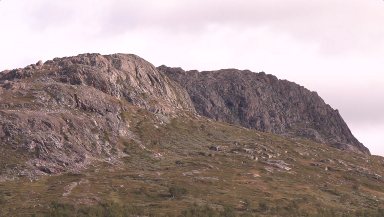 Ett bergigt landskap med klippor och grön vegetation under en molnig himmel.