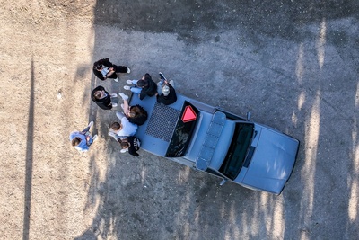 Fågelperspektiv av en grupp människor som står vid en bil på en grusväg.