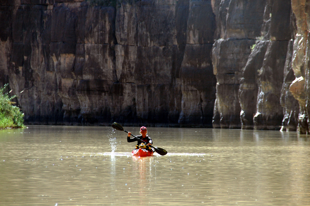 En person paddlar kajak på en lugn flod omgiven av höga klippväggar.