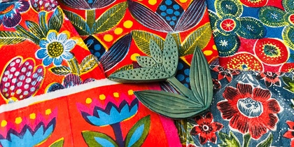 Färgglada tyger med blommönster och två gröna bladformade stämplar ovanpå.