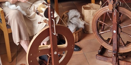 En person spinner garn med en spinnrock i ett vardagsrum med soffor och bord.