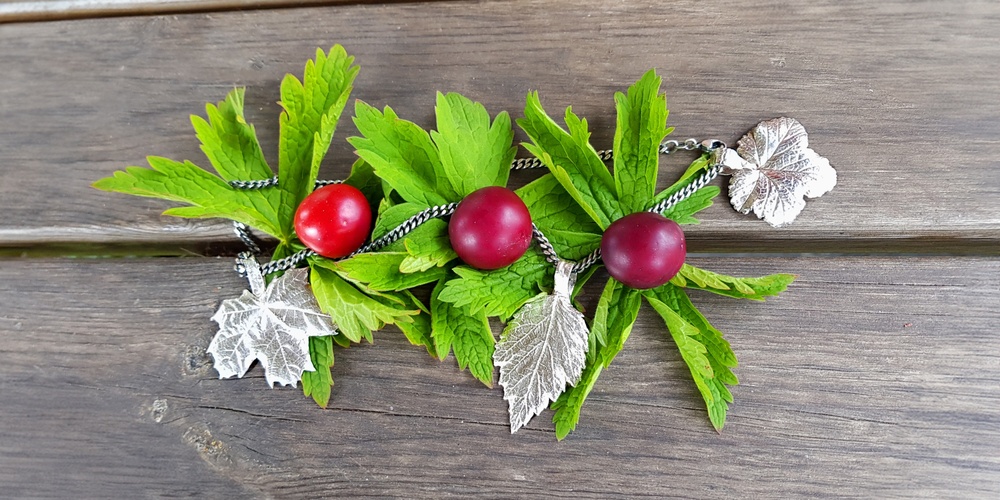 En dekoration med gröna blad, röda bär och silvriga löv ligger på ett träbord.