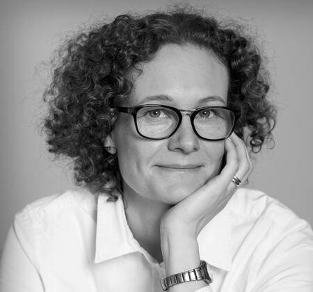 Person med lockigt hår sitter med handen mot kinden, bär vit skjorta och armbandsur.