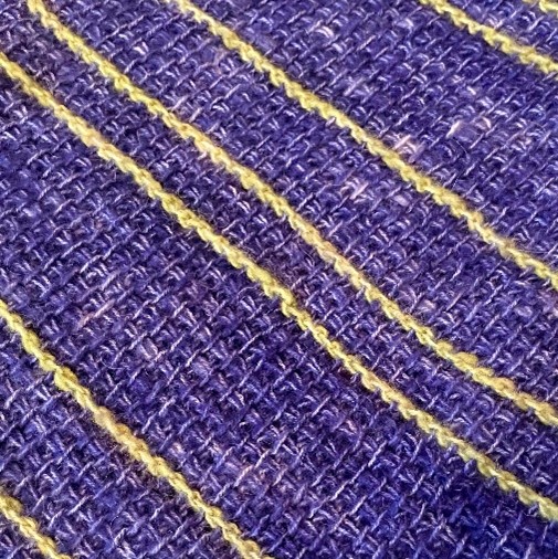 Närbild av ett vävt tyg i lila med gula ränder och grov struktur.