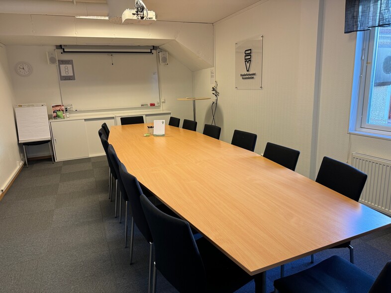 Ett modernt konferensrum med långbord, svarta stolar, whiteboard och fönster.