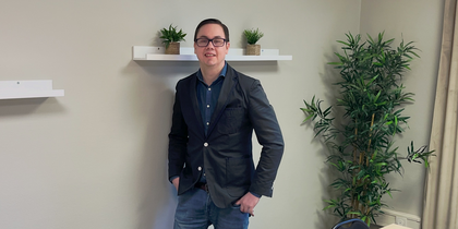 En person står vid väggen i ett mötesrum med bord, stolar, växter och hyllor med krukväxter.