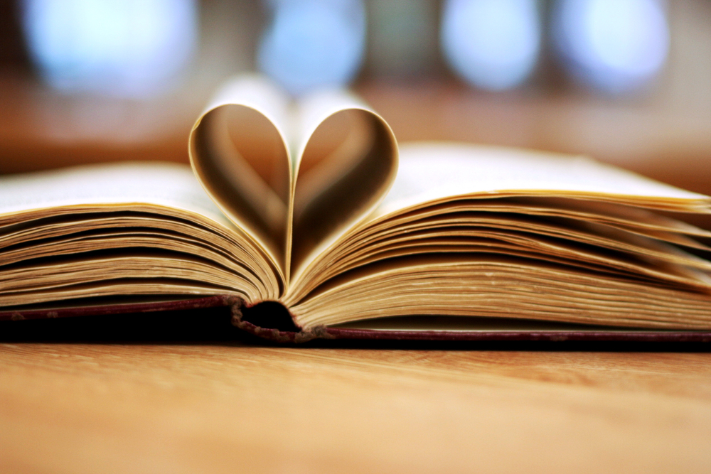 En öppen bok med två sidor vikta till ett hjärta, liggande på ett träbord.