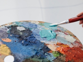 En person håller en pensel och en färgpalett fylld med olika färger, redo att måla.