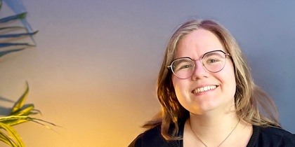 Två leende personer sitter tillsammans i en blå soffa i ett rum med blå vägg och grön växt.