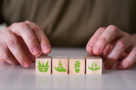 Två händer placerar träklossar med gröna miljöikoner på ett bord.