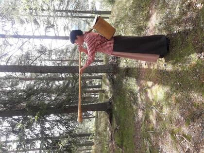 En person i traditionella kläder blåser i en lång trätuta i en skog.