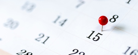 Närbild av en kalender med färgade nålar som markerar viktiga datum.