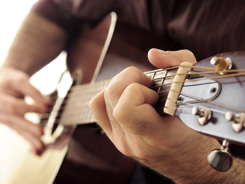 Närbild av en person som spelar akustisk gitarr, fokus på vänster hand på gitarrens greppbräda.